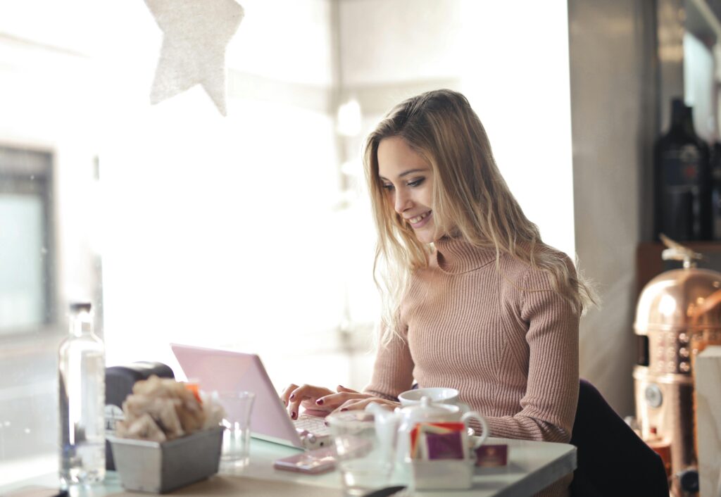 Smiling woman using laptop in bright cafe setting with coffee and pastries.